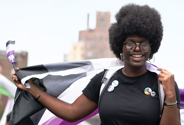 A Black person holds a large ace flag behind them and a smaller ace flag in their outstretched right hand.